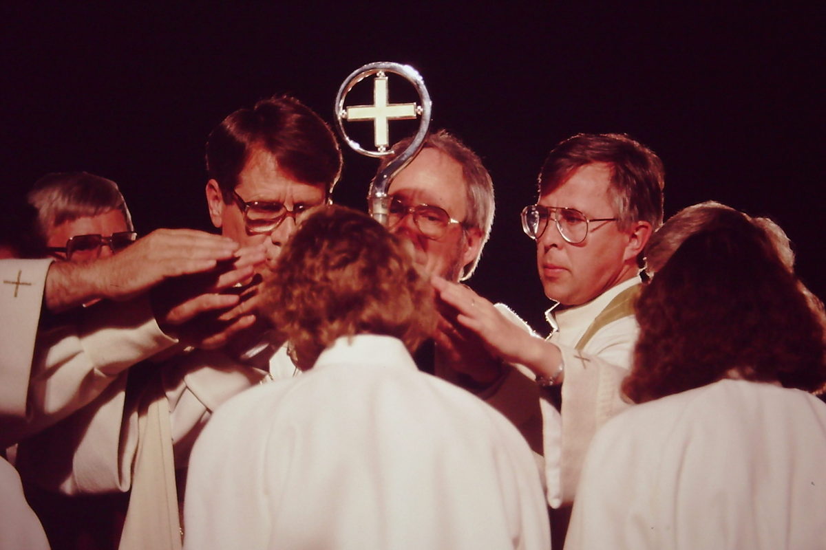 Joukko pappeja siunaa nuorta naista kädet hänen päänsä yllä.
