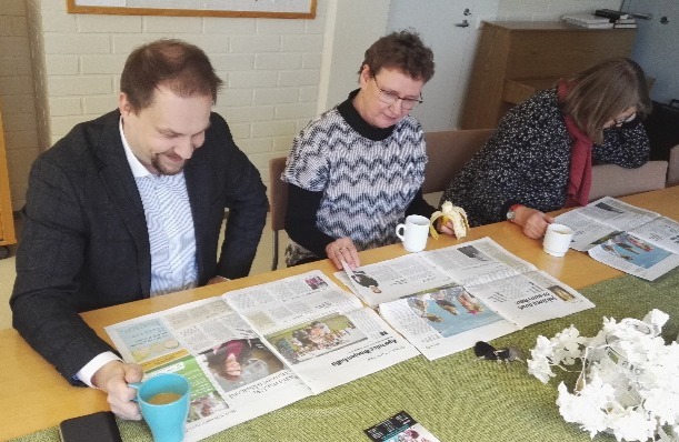 Kolme henkilöä lukee pöydän ääressä Risteys-seurakuntalehteä.