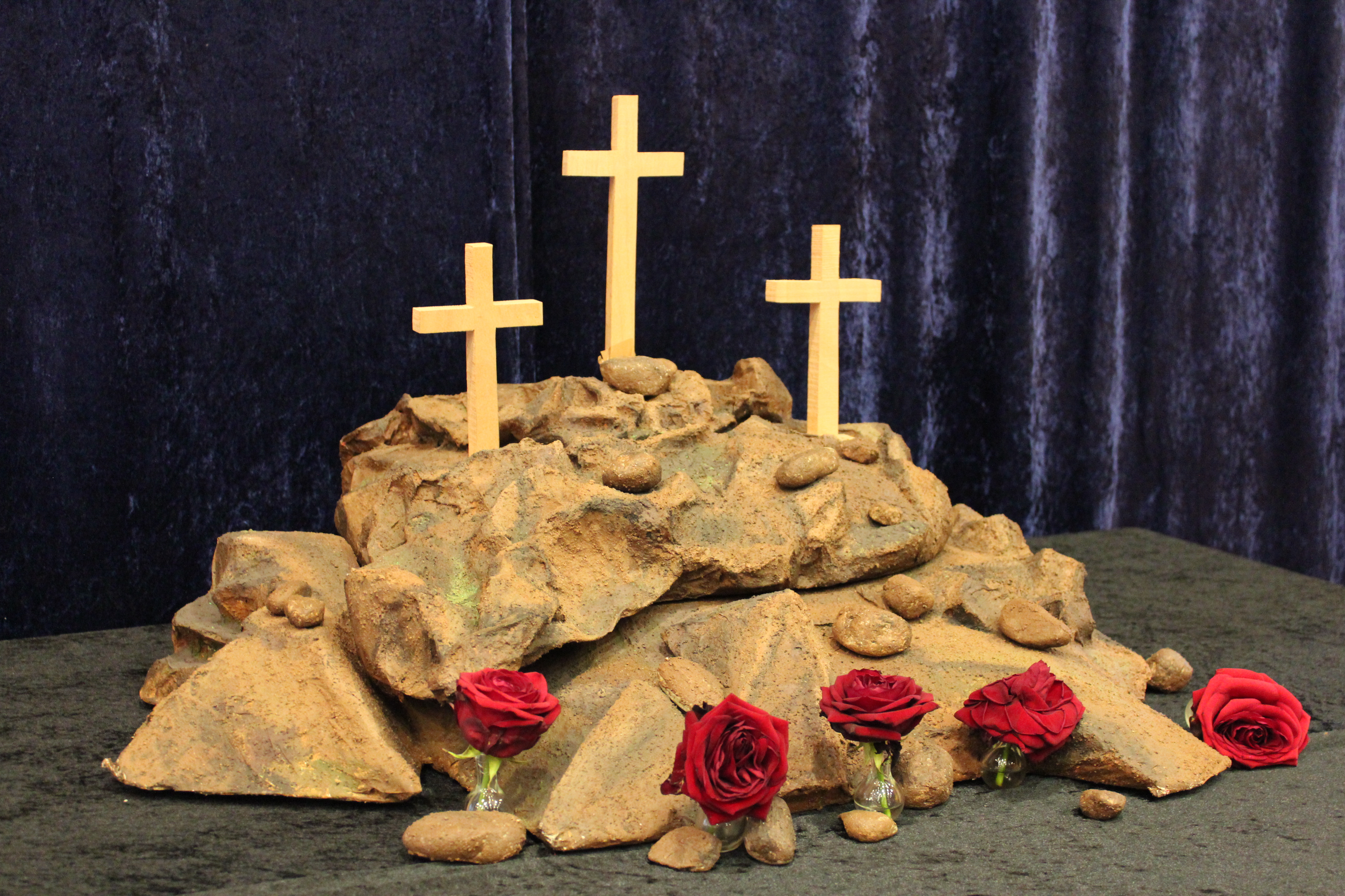 Pääsiäisalttari. Kolme ristiä kivikummun päällä ja edessä punaisia ruusuja.