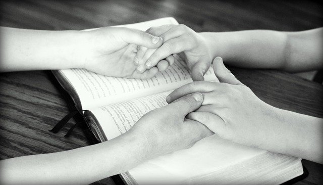 Kaksi naista pitää toisiaan käsistä avonaiset Raamatun päällä