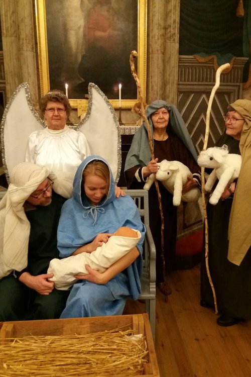 Maria, Joosef ja Jeesus-lapsi seimen äärellä enkelin ja paimenten kanssa.