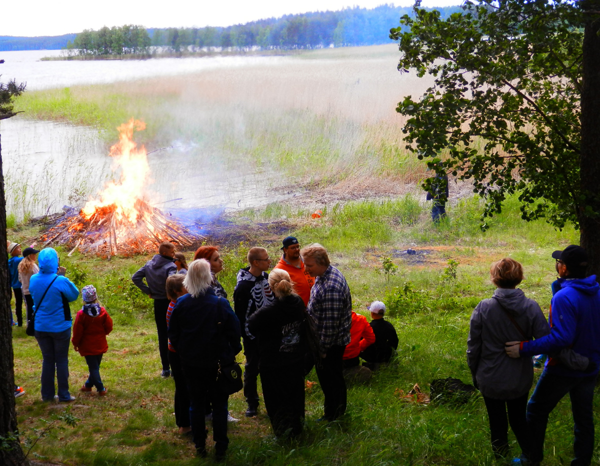 Juhannuskokko palaa järven rannalla Valkealan Niinirannassa. Ympärille kerääntynyt ihmisiä katsomassa kokkoa.
