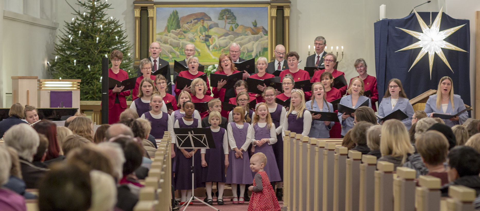 Kirkko täynnä ihmisiä laulamassa Kauneimpia Joululauluja