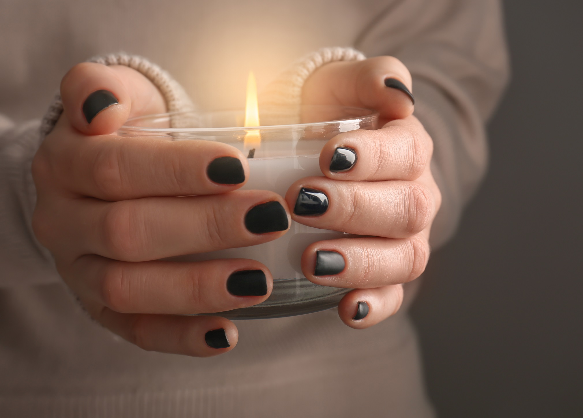Nuoren naisen käsissä on palava kynttilä.