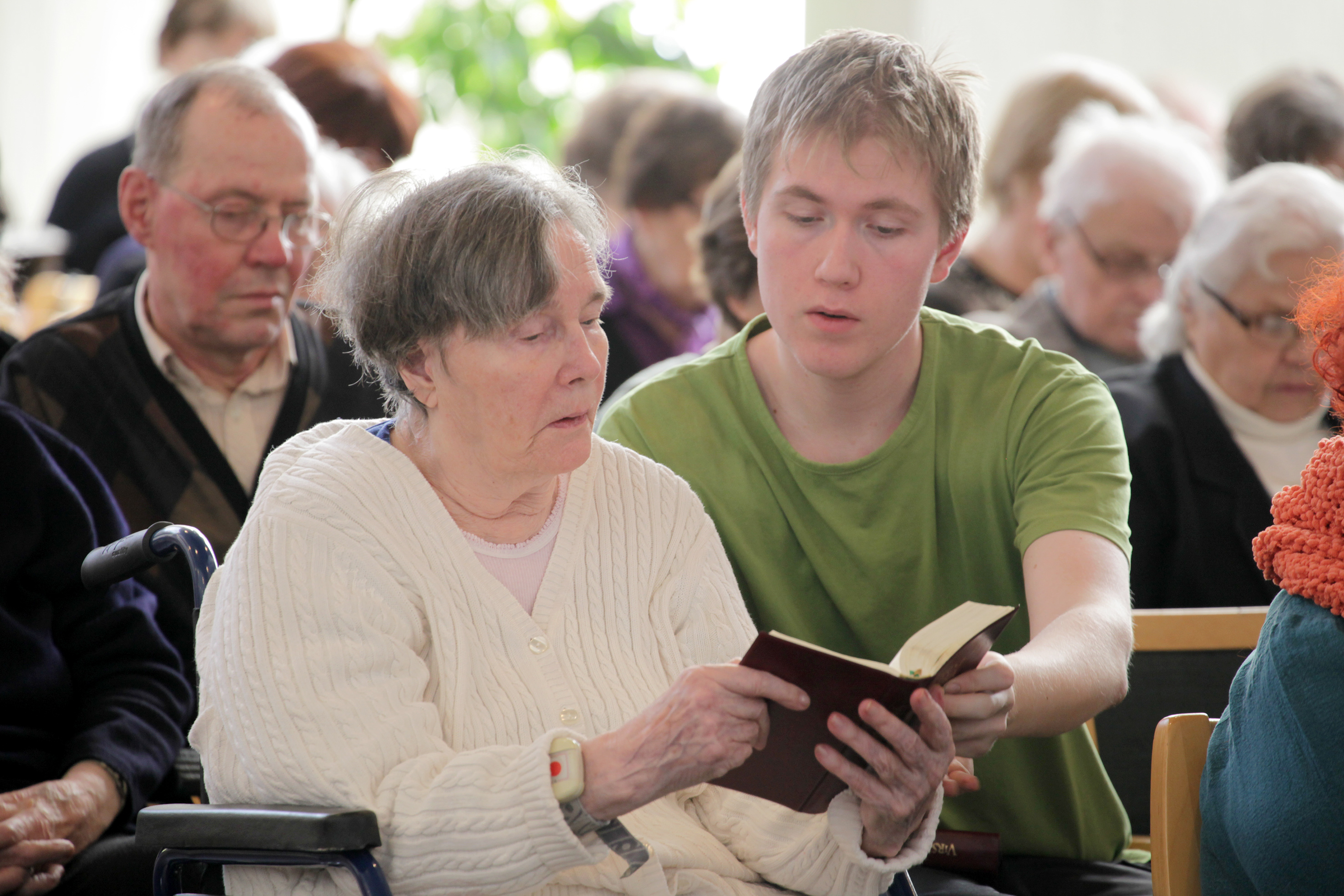 Kirkossa vanhempi nainen ja nuori mies pitelevät yhdessä virsikirjaa.