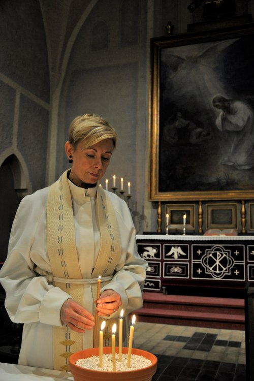 Seurakuntapastori Satu Leino on Kuusankosken kirkon alttarin edustalla sytyttämässä pyhäinpäivän kynttilöitä.
