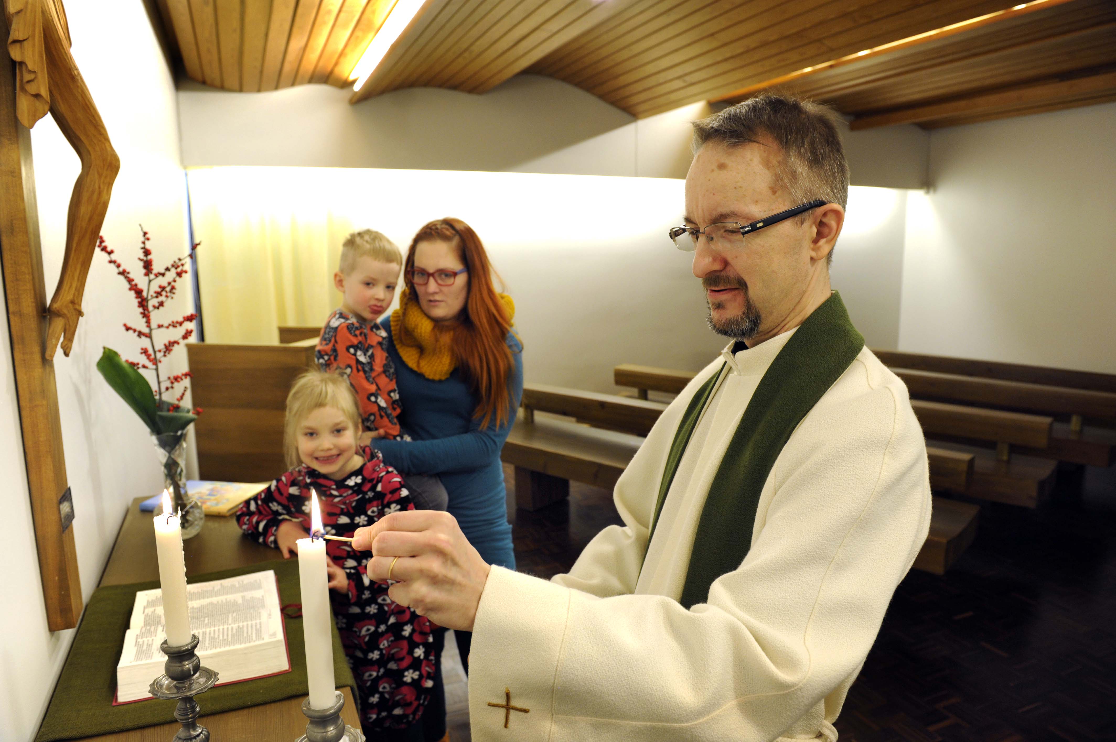 Äiti ja lapset seuraavat, kun pappi sytyttää kappelin alttarille kynttilän.