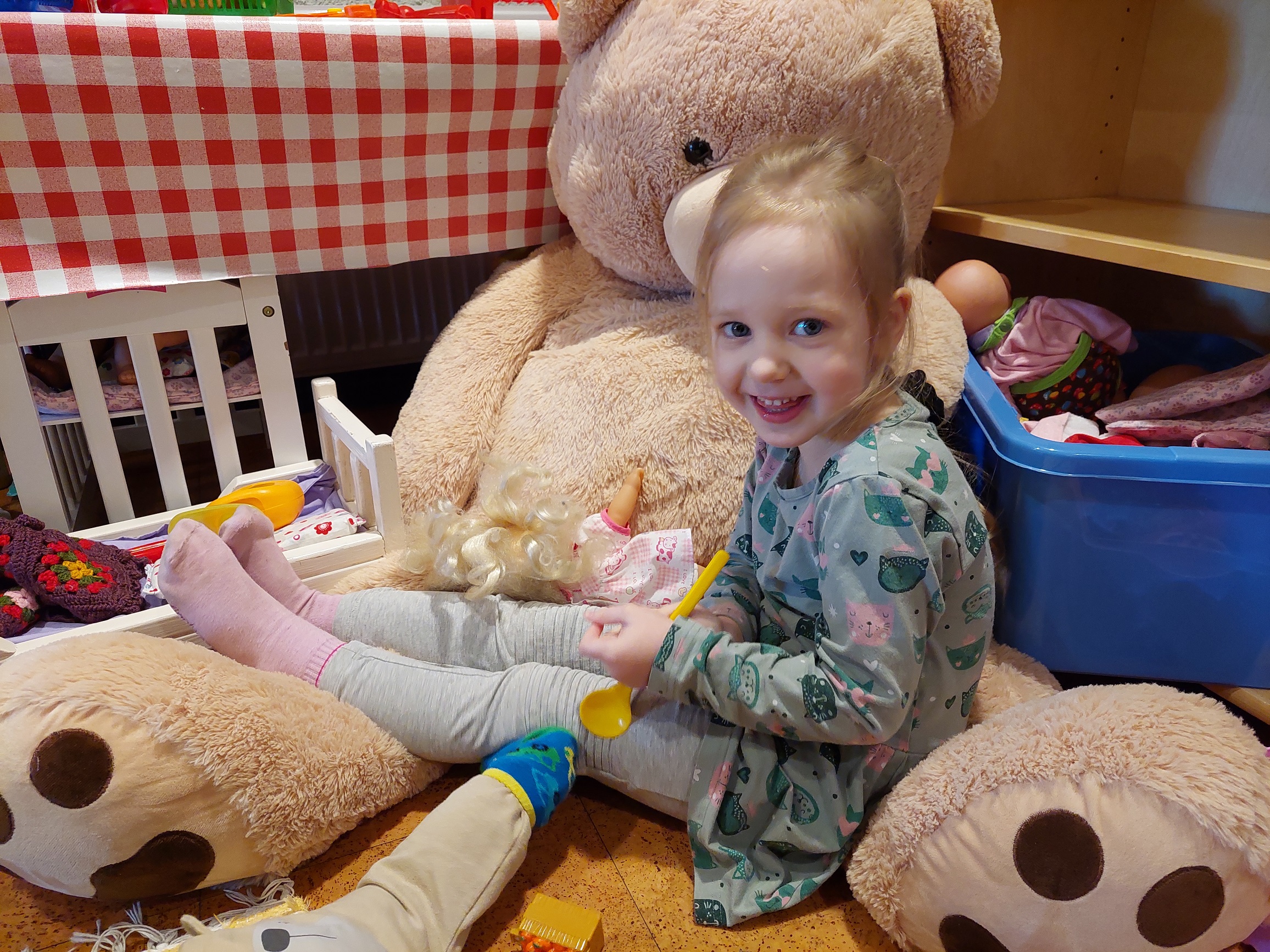 Pieni tyttö istuu leikkimässä ison lelunallekarhun sylissä.
