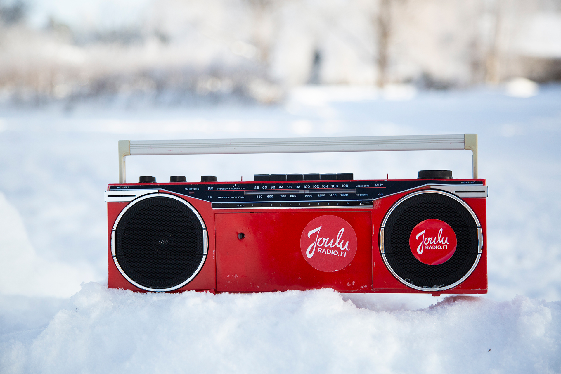 Punainen retro radio lumihangossa. Radiossa on punainen tarra, jossa lukee Jouluradio.