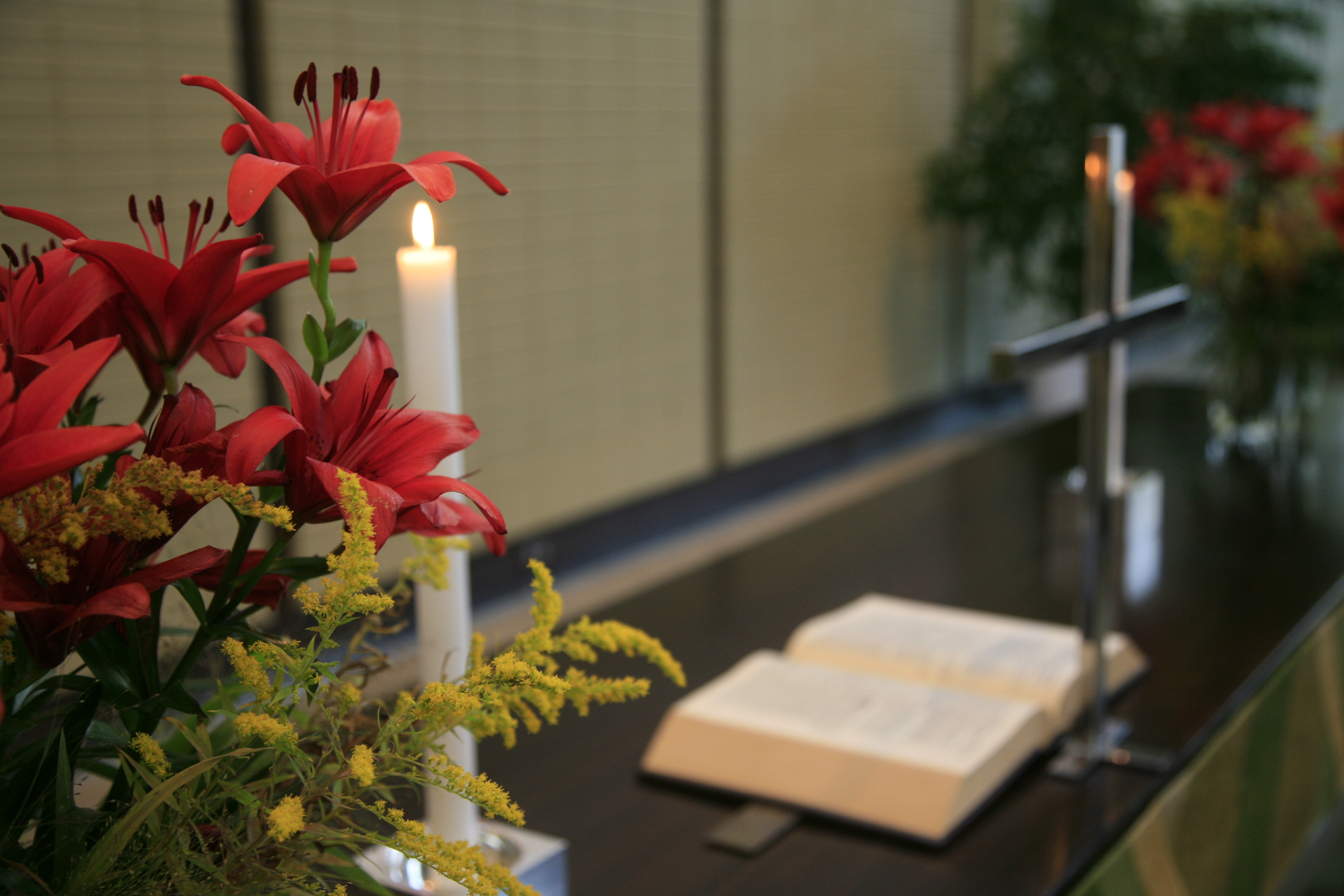 Kirkon alttarilla kukkia, kynttilöitä ja avonainen Raamattu.