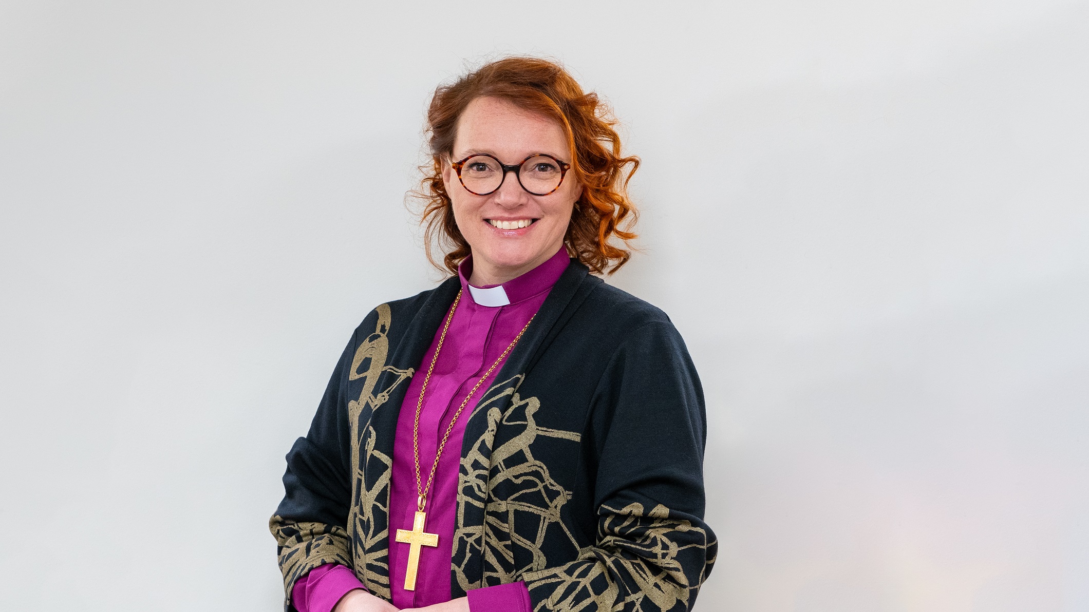 Piispa Mari Parkkinen hymyilevänä, violetissa virkapaidassaan.