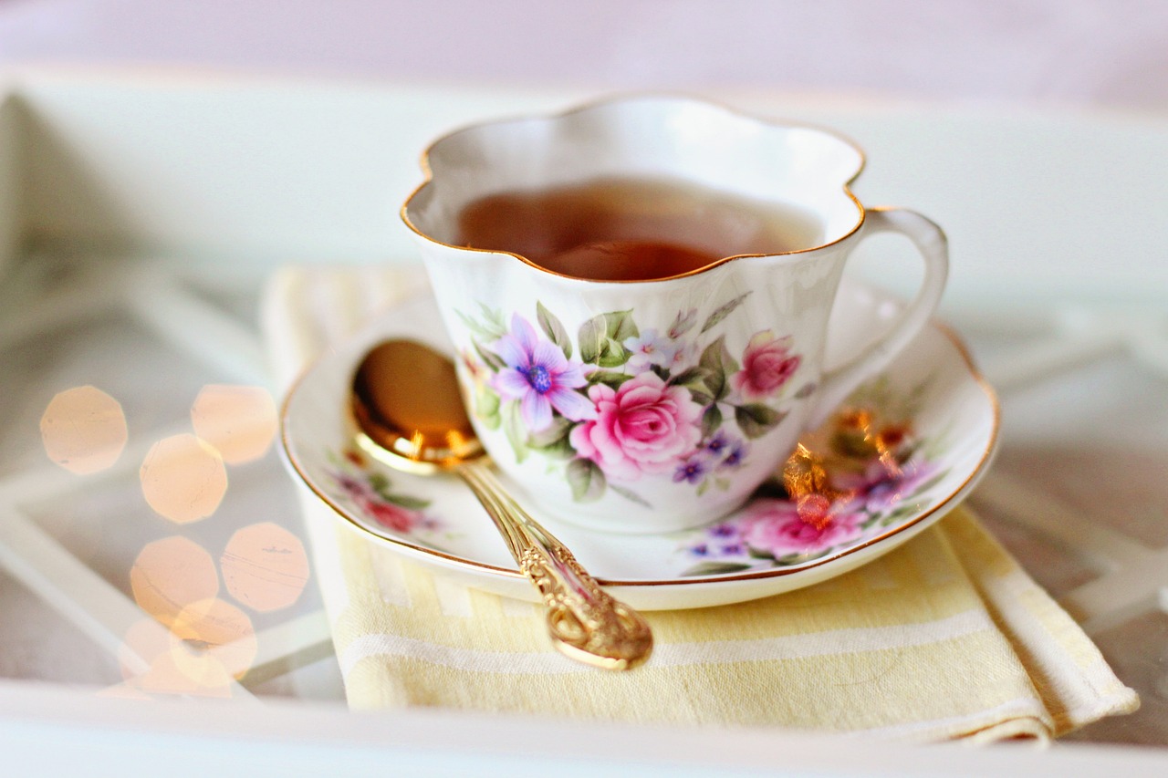 Kukkakuvioinen pieni teekuppi täynnä teetä, ja asetti, jolla on kultainen lusikka.